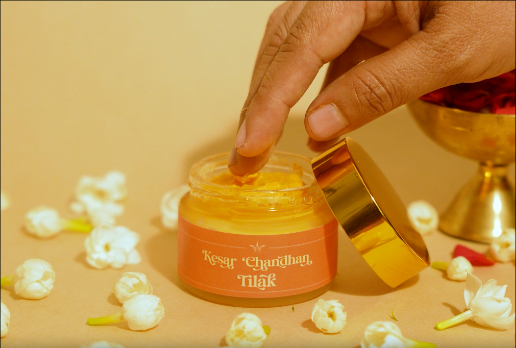 Hand taking a small amount of Deiveegaa Kesar Chandhan Tilak paste from the jar